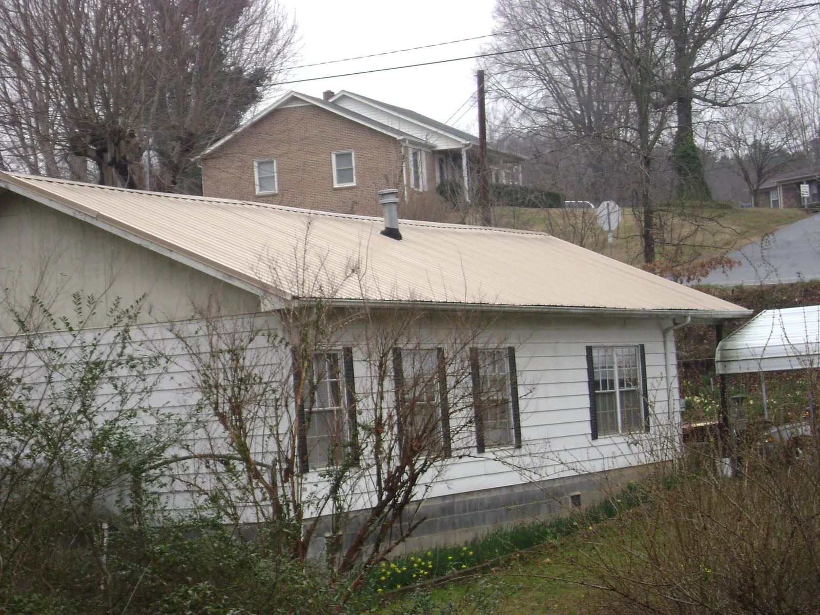 Tan metal roof on a white sided house set into a hillside — Commercial Roofing by Roofing Brothers in Palmetto